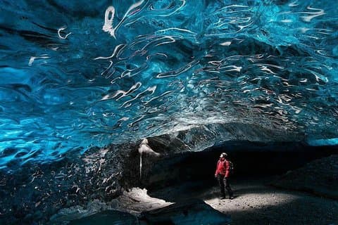 A person marvels at the blue ice walls inside an ice cave in Iceland.