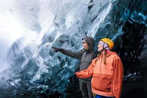 A man and a woman admire icy formations inside an ice cave in Iceland.