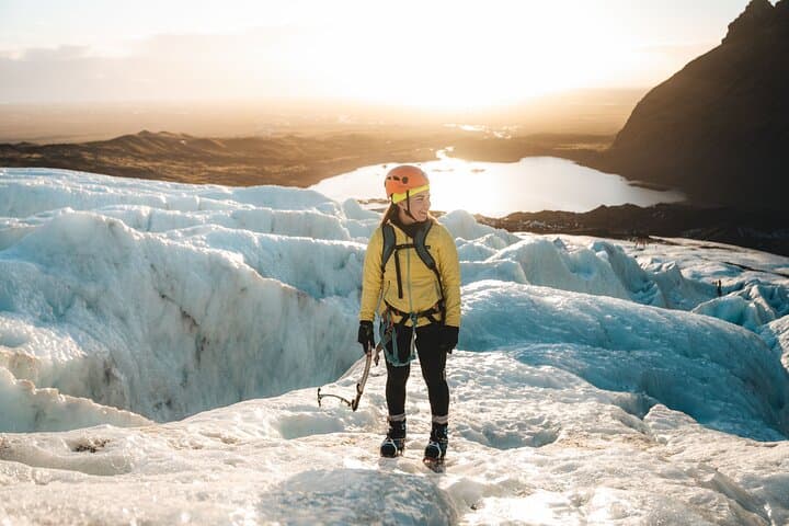 A person wearing an orange helmet and yellow jacket smiles while pausing during a glacier hike.