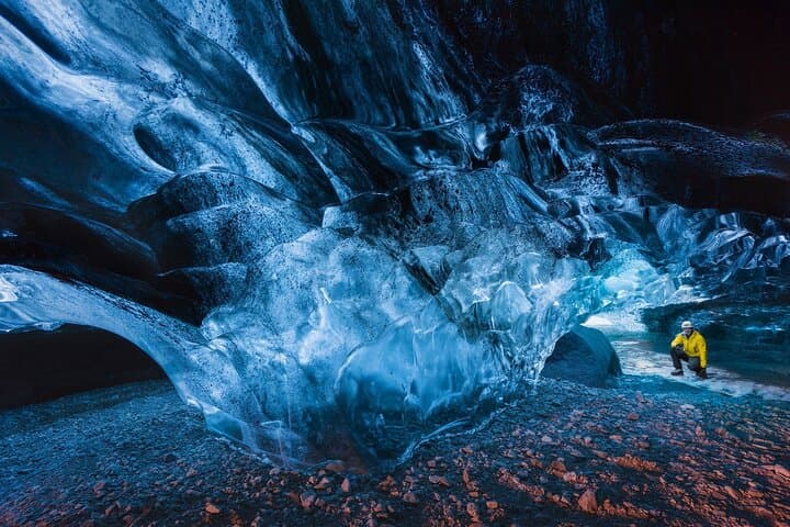 Visitors explore a natural ice cave in Iceland with blue ice walls surrounding them.