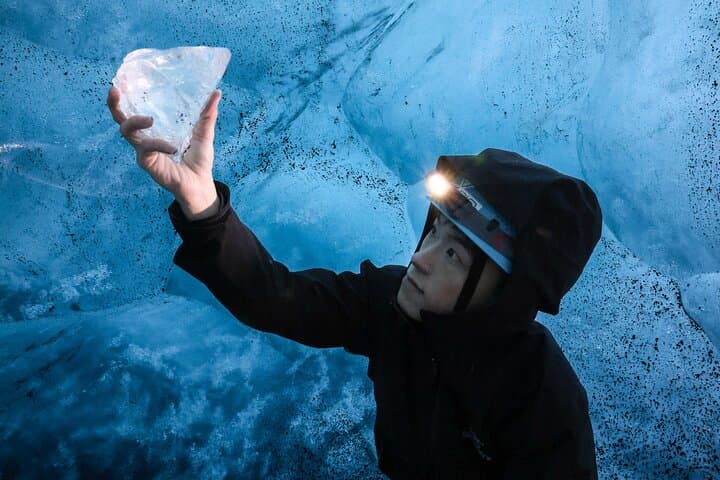 A visitor in an ice cave examines a piece of ice in their hand.